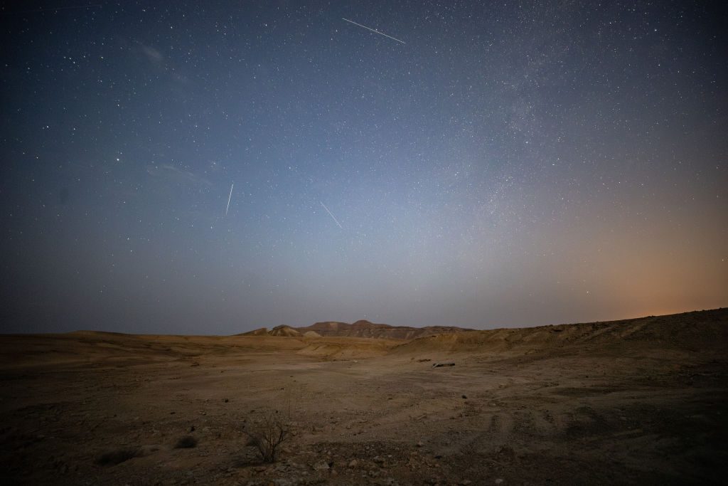 Numerosos meteoros atraviesan el cielo estrellado sobre un paisaje desértico árido.
