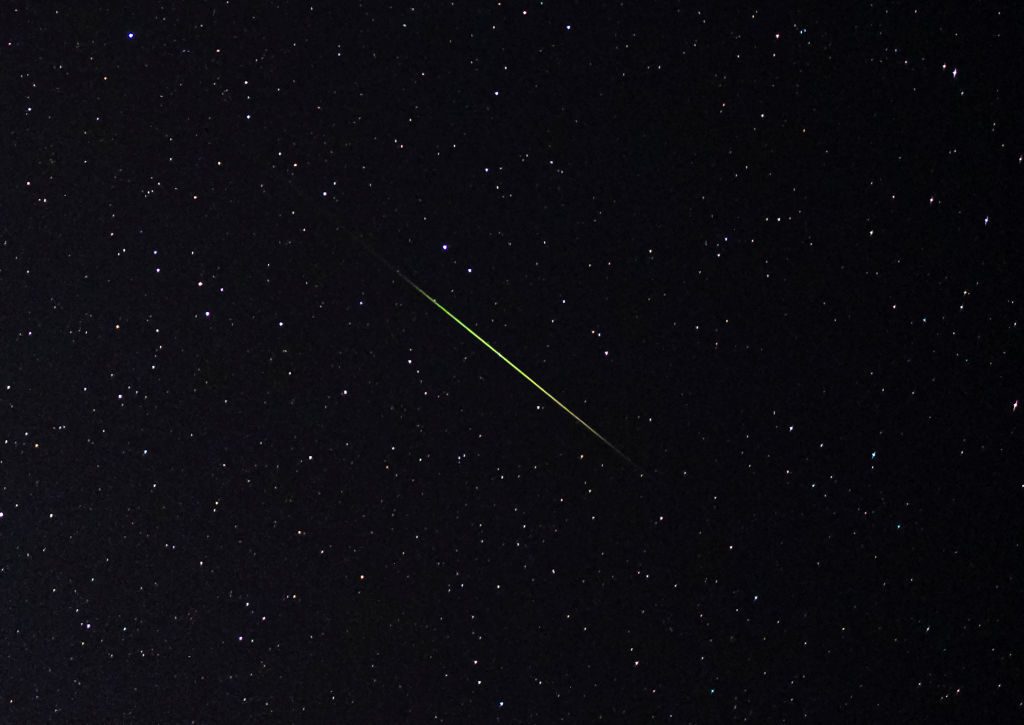 Primer plano de una racha de meteoritos de color verde brillante y blanco a través de un cielo estrellado.