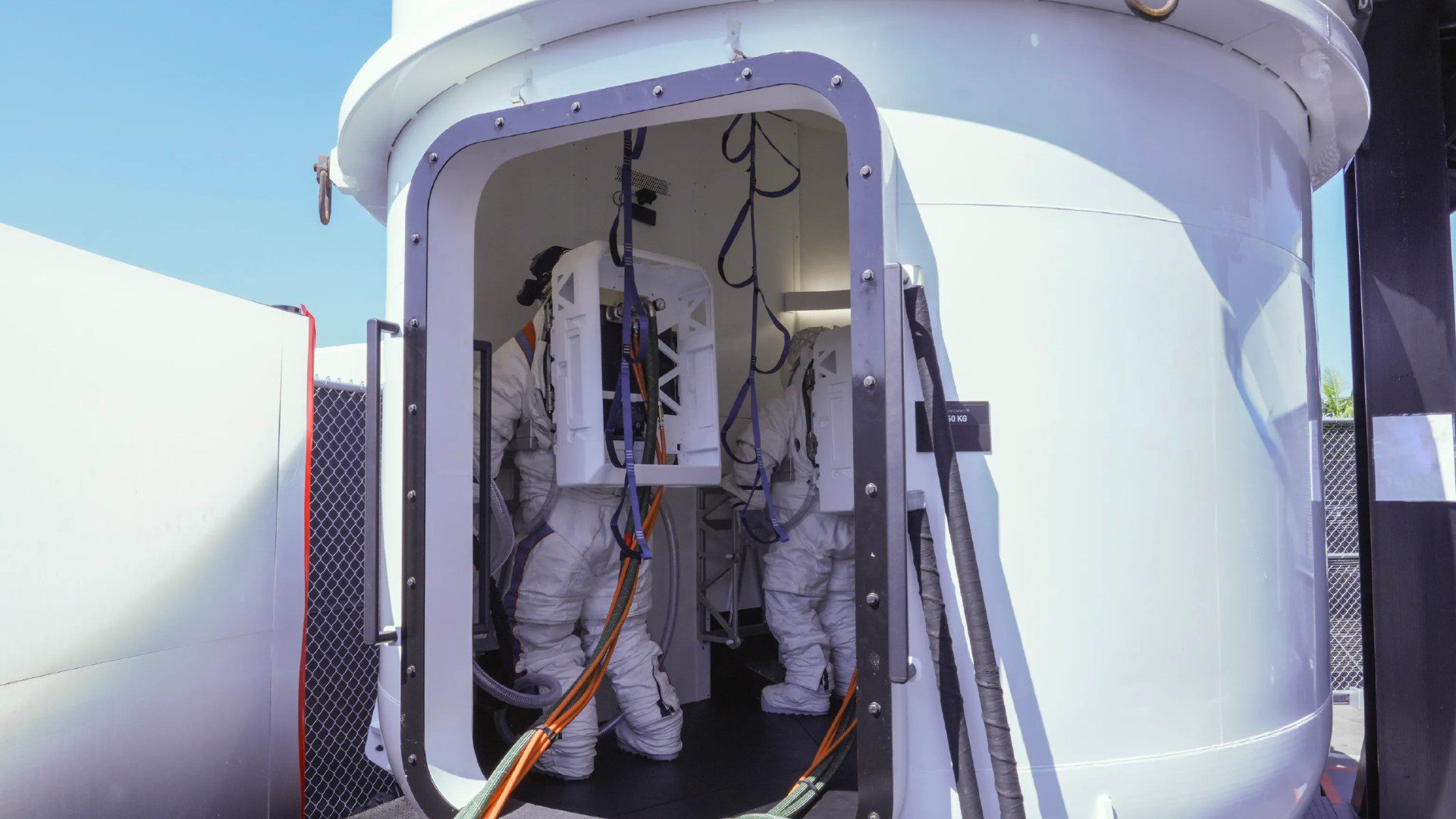 Astronautas con trajes espaciales blancos se encuentran dentro de una esclusa de aire blanca