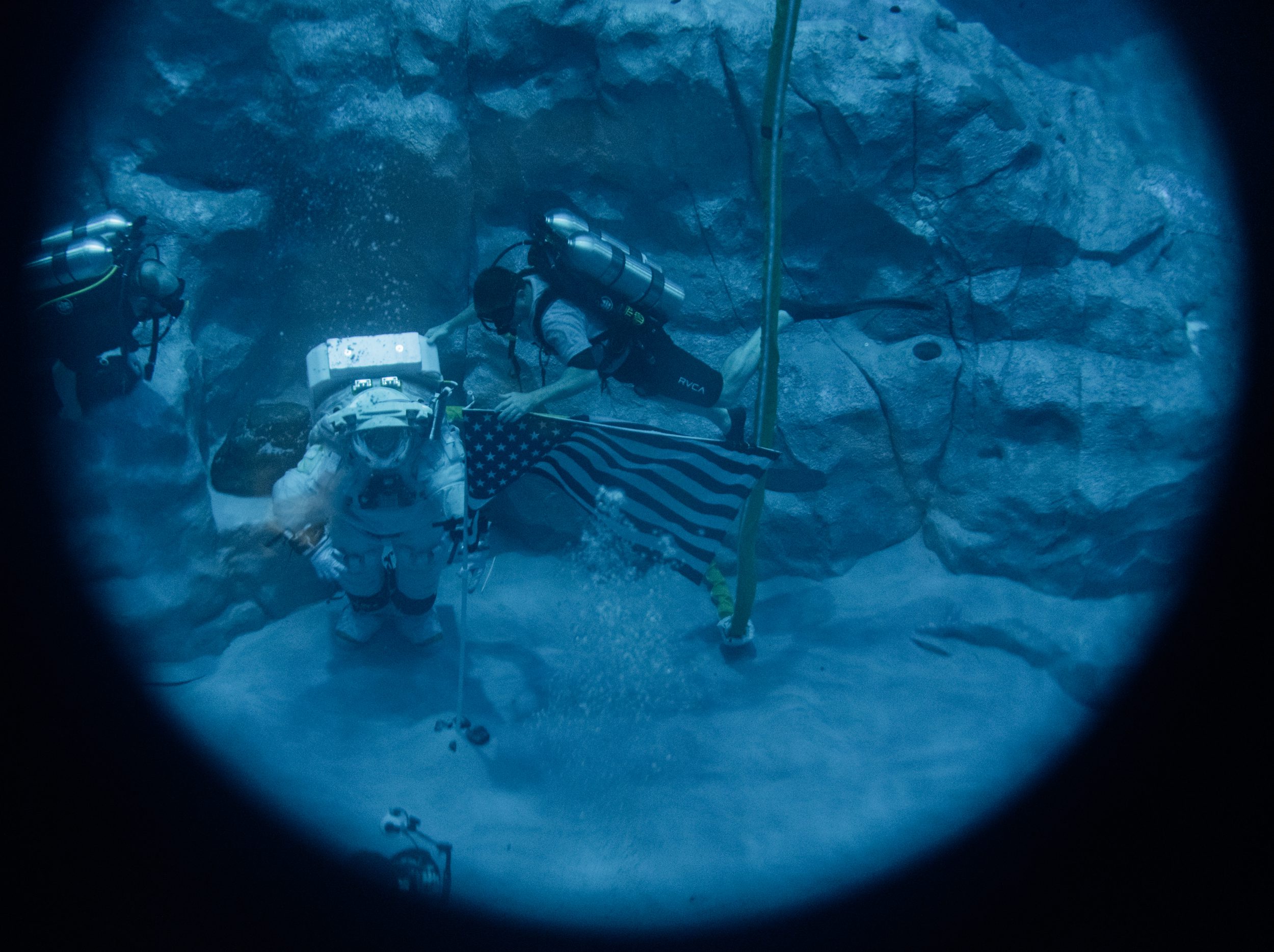 Un astronauta con traje espacial camina sobre el fondo de una piscina junto a un buzo con máscara de buceo