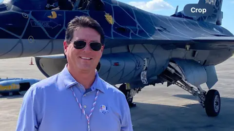 Fred López se para frente a un avión de combate, vestido de civil.