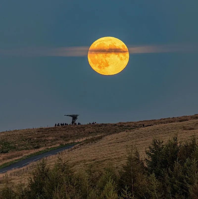 La Luna de la Cosecha diseccionada por una nube el 18 de septiembre de 2024, tomada por Lee Mansfield sobre la escultura Singing Ringing Tree, Burnley, Lancashire, Reino Unido. El Singing Chime Tree es una escultura acústica impulsada por el viento que se asemeja a un árbol ubicada en el paisaje de Pennine Hills con vistas a Burnley, en Lancashire.