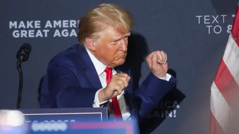 Donald Trump viste un traje azul y corbata roja y baila mientras sale del escenario durante un mitin de campaña en New Hampshire.