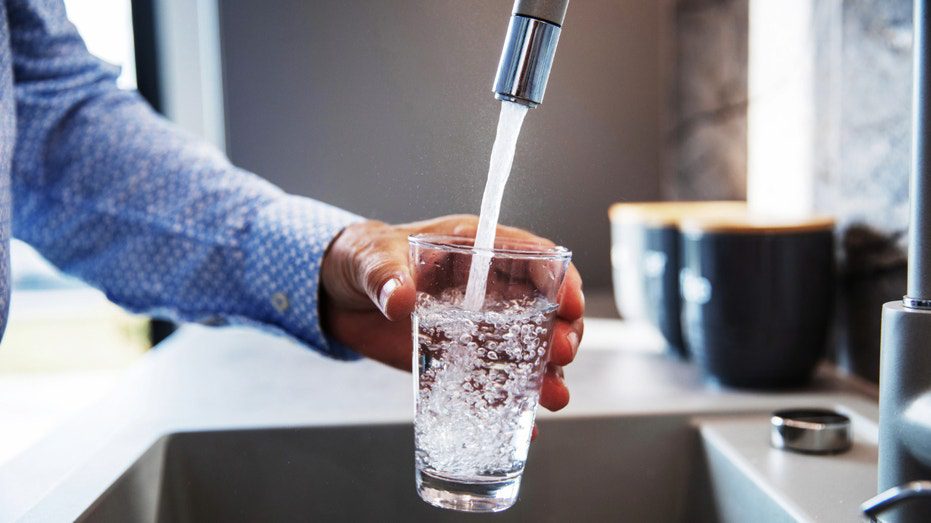 Una persona llena una taza con agua del fregadero de su casa.