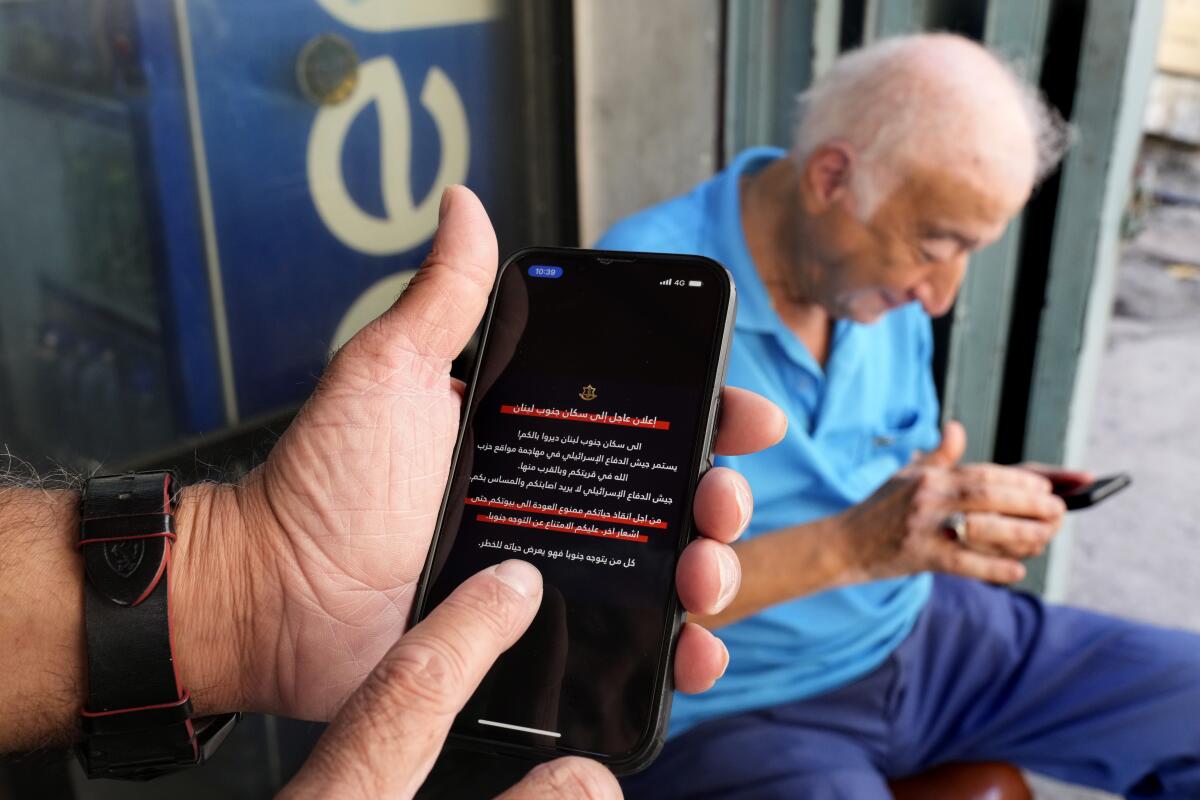 Hombres leen alertas de teléfonos móviles que dicen a los residentes del sur del Líbano que no regresen 