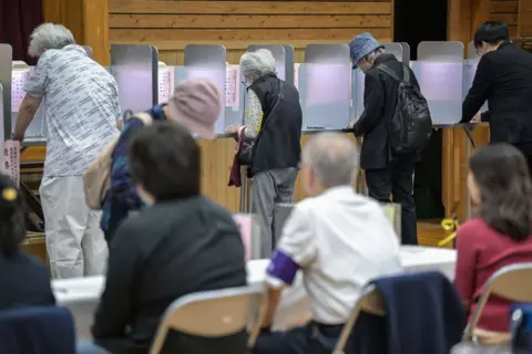 Getty Images Los funcionarios observan cómo la gente vota durante las elecciones generales en un colegio electoral instalado en una escuela local en Tokio el 27 de octubre de 2024.